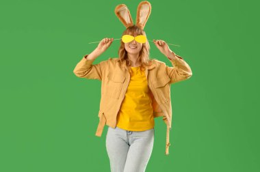 Paskalya tavşanı kulaklı ve yeşil arka planda kağıt yumurtası olan genç bir kız.