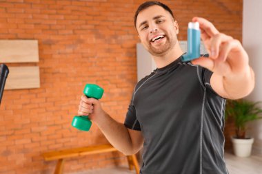 Spor salonunda astım spreyi ve halterli genç bir adam.