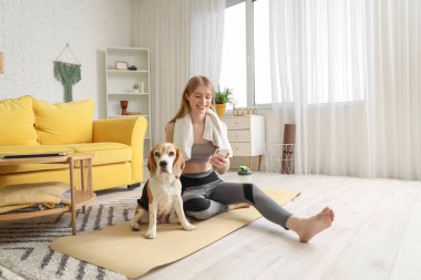 Evde yoga yaptıktan sonra sevimli Beagle köpeği ve cep telefonu olan genç bir kadın.