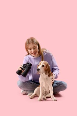 Dürbünlü genç kadın ve pembe arka planda oturan Beagle köpeği.