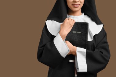 Kahverengi arka planda İncil 'i olan genç rahibe, yakın plan.