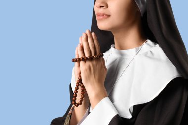 Mavi arka planda dua eden tespih taşıyan genç bir rahibe.