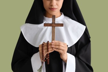 Yeşil arka planda haç ve tespih taşıyan genç rahibe, yakın plan.