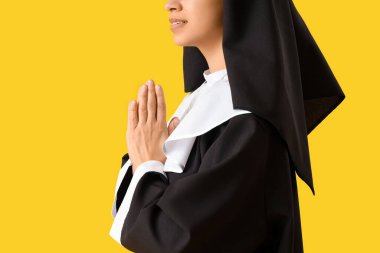 Genç rahibe sarı arka planda dua ediyor.