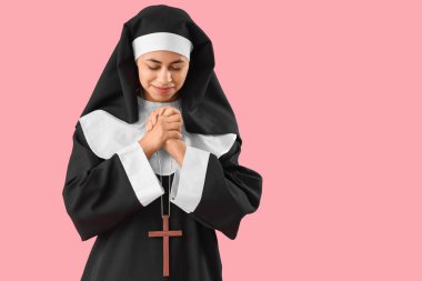 Genç rahibe pembe arka planda dua ediyor.