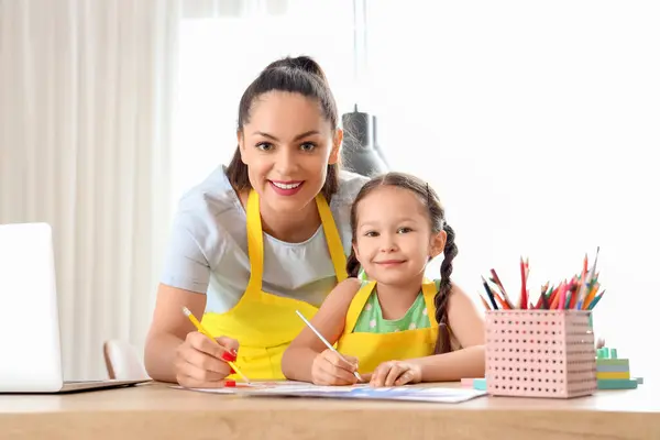 Little girl with her working mother drawing in kitchen