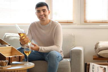 Evde şarap şişesi olan genç bir adam var.