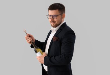 Genç şarap garsonu gri arka planda şarap şişesi açıyor.