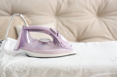 Beyaz tişörtlü elektrikli ütü odada, yakın plan.