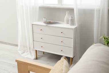 Oturma odasının penceresinin yanında vazo ve bardaklı çekmeceler.