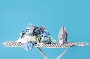 Mavi arka planda bir yığın elbisesi olan elektrikli ütü.