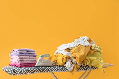 Sarı arka planda giysileri olan elektrikli ütü.