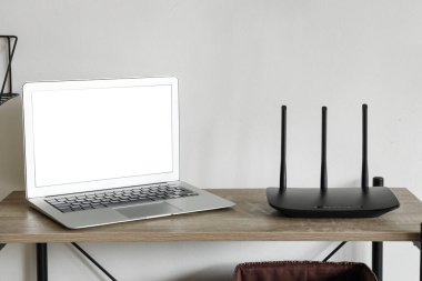 Işık duvarının yanında boş dizüstü bilgisayarı olan modern wi-fi yönlendirici