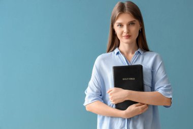 Kutsal kitabı olan genç bir kadın mavi arka planda dua ediyor.