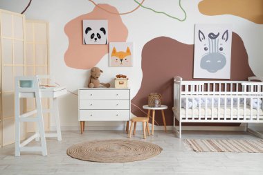 Çocukların yatak odasının içinde resimler, bebek beşiği ve değişen masa var.