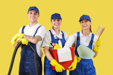 Sarı arka planda malzemeleri olan temizlik işçileri.