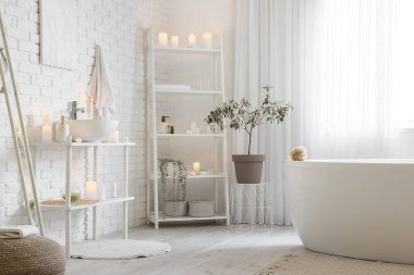 İçinde yanan mumlar, lavabo ve raf ünitesi olan şık bir banyo.