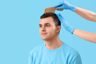 Doktor mavi arka planda genç adamın saçını tarıyor, yakın plan.