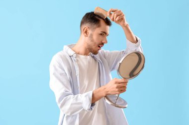 Şok olmuş genç esmer adam saç dökülmesi sorunu ve mavi arka planı taraması