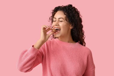 Güzel bir Afro-Amerikalı kadın pembe arka planda çikolata yiyor.