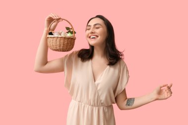 Paskalya sepetini pembe arka planda dekoratif kozmetik ürünleriyle tutan mutlu genç kadın.