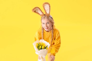 Paskalya tavşanı kulakları, çiçekleri ve sarı arka planda kağıt yumurtası olan genç bir kız.