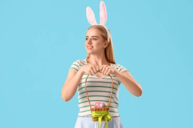 Tavşan kulaklı genç kız ve mavi arka planda Paskalya sepeti