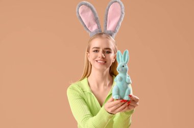 Paskalya tavşanı kulaklı ve bej arka planda oyuncak tavşanı olan genç bir kız.