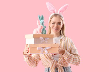 Paskalya tavşanı kulaklı genç kız, oyuncak tavşanlar ve pembe arka planda hediyeler.