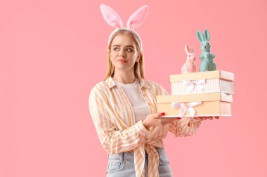 Paskalya tavşanı kulaklı genç kız, oyuncak tavşanlar ve pembe arka planda hediyeler.