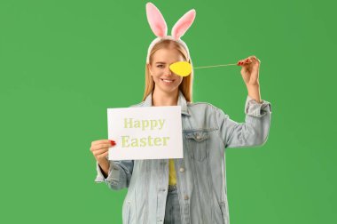 Paskalya tavşanı kulaklı genç bir kız, yeşil arka planda tebrik kartı ve kağıt yumurta.