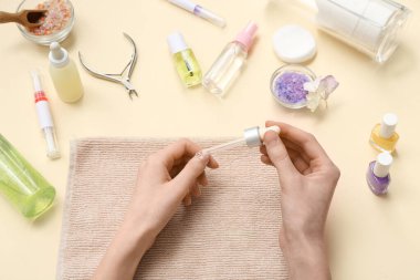 Bej arka planda deri altı yağı, şişe ve havlu bulunan pipeti tutan kadın eller.