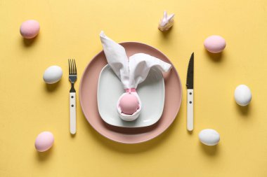 Sarı arka planda boyanmış yumurtalarla Paskalya kutlaması için masa ayarlayın. Üst görünüm