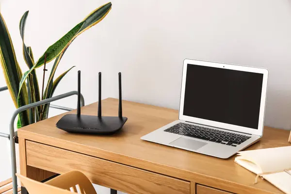 Modern wi-fi router with laptop on table near light wall