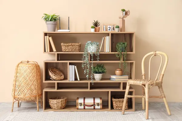 Bookshelf with modern wi-fi router and plants near beige wall in room