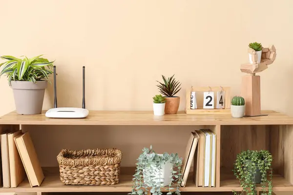 Modern wi-fi router with plants on shelf near beige wall