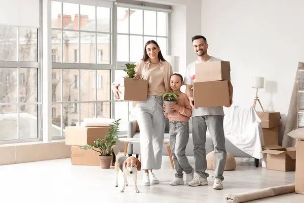 Happy family with cardboard boxes and Beagle dog in room on moving day
