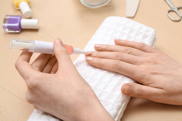 Female hands applying cuticle oil onto fingernails on beige background