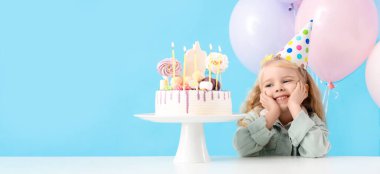 Parti şapkalı şirin küçük kız ve masada doğum günü pastasıyla mavi arka planda mesaj için yer var.