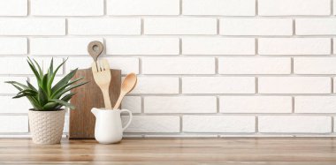 Mutfak gereçleri ve ev bitkileri beyaz tuğla duvarın yanındaki ahşap tezgahta. Tasarım için pankart