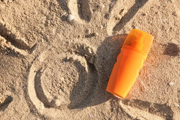 Creative composition with bottle of sunscreen cream on sand at sea beach