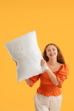 Turuncu arka planda beyaz yumuşak yastıklı mutlu genç kadın.