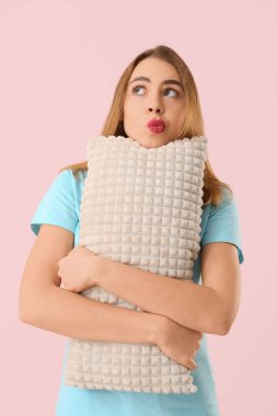 Pembe arka planda yumuşak yastıklı düşünceli genç bir kadın.