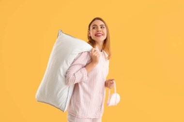 Beyaz yumuşak yastıklı ve turuncu arka planda uyku maskeli güzel bir kadın.