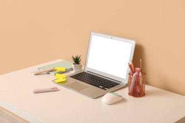 Ofisteki masada dizüstü bilgisayar, bilgisayar faresi, kalem tutacağı ve defter.