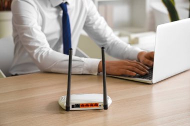 Ofiste dizüstü bilgisayar kullanan iş adamının masadaki modern Wi-Fi yönlendiricisi.