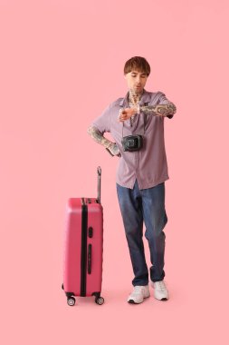 Çantalı bir erkek turist pembe arka planda kol saatine bakıyor.