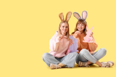 Paskalya tavşanı kulaklı genç kızlar ve sarı arka planda kağıt tavşanlar.