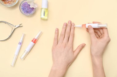 Bej arka planda deniz tuzu ve kesicili tırnak eti yağı kalemi tutan kadın eller.