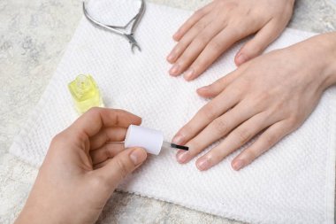 Manikür ustası gri grunge arka planda kadın tırnaklarına manikür yağı sürüyor.